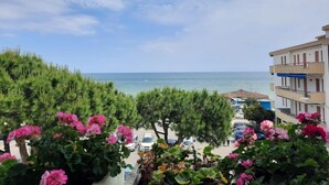A coastal view with a building, parked cars, and flowering plants. - Hotel Giada (Silvi)