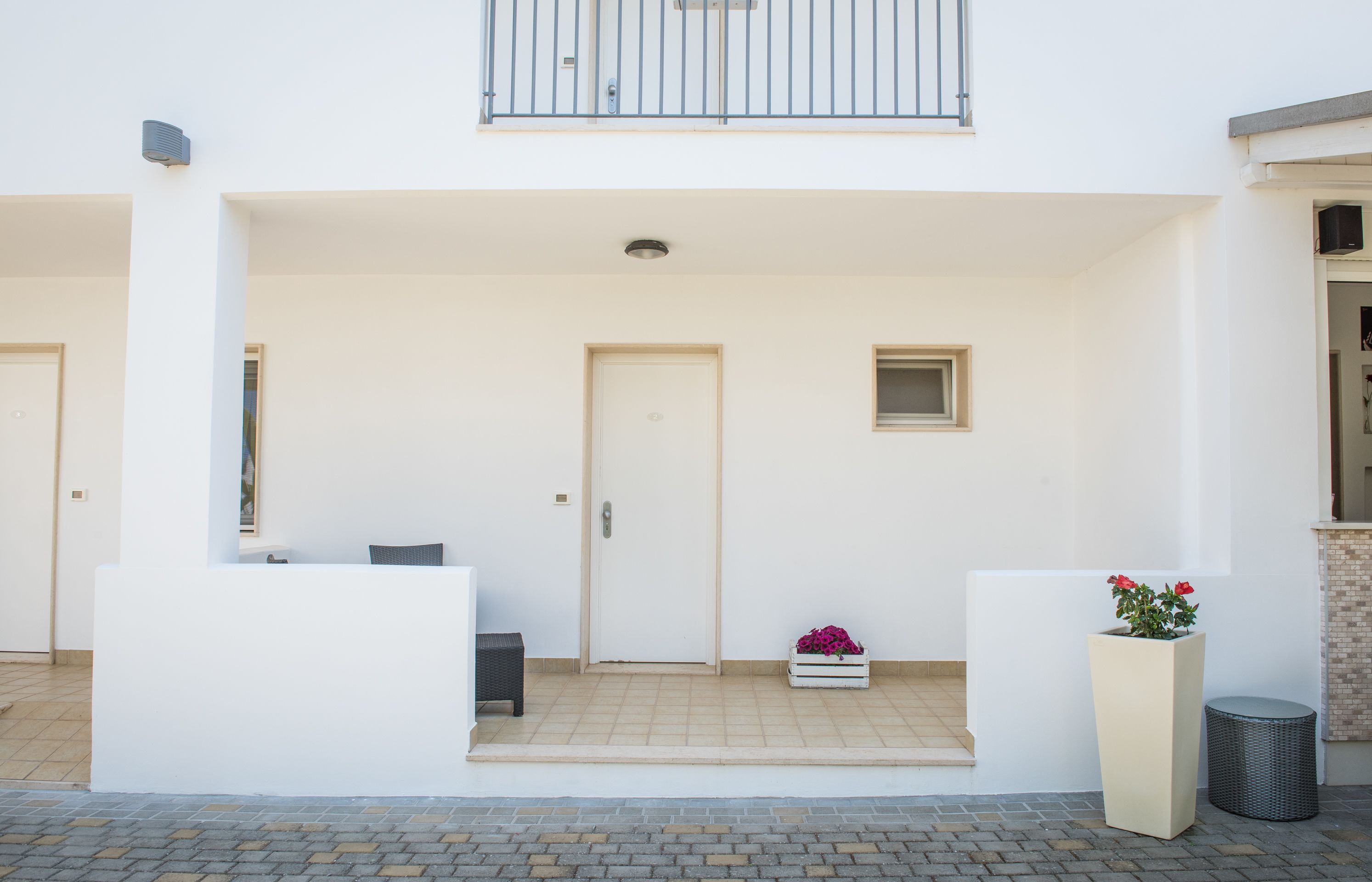A modern building with a white facade, a balcony, a door, and a small window.