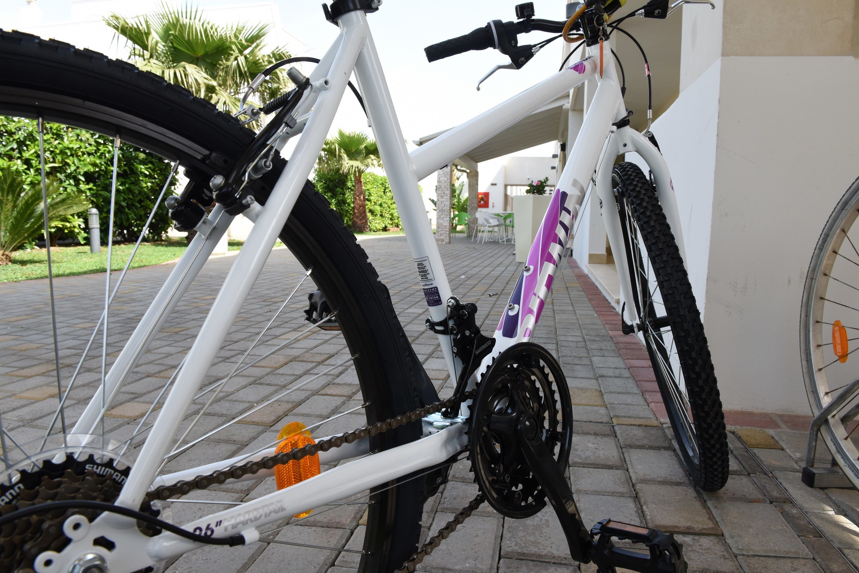 A white bicycle with a purple and black frame parked on a paved surface.