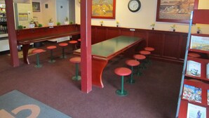 Un restaurante con una barra alargada, varios taburetes, un banco y un reloj en la pared.