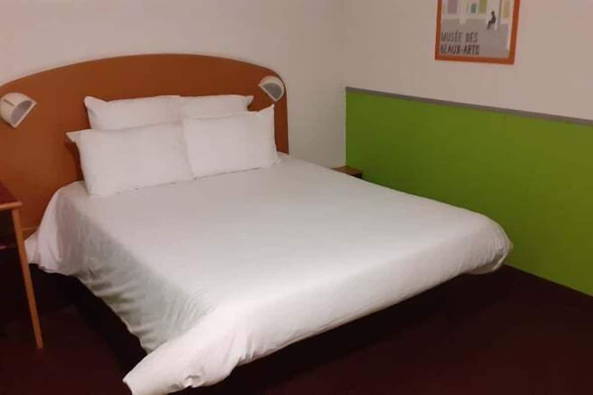 Un lit avec une literie blanche, une tête de lit en bois et un mur d’accent vert.