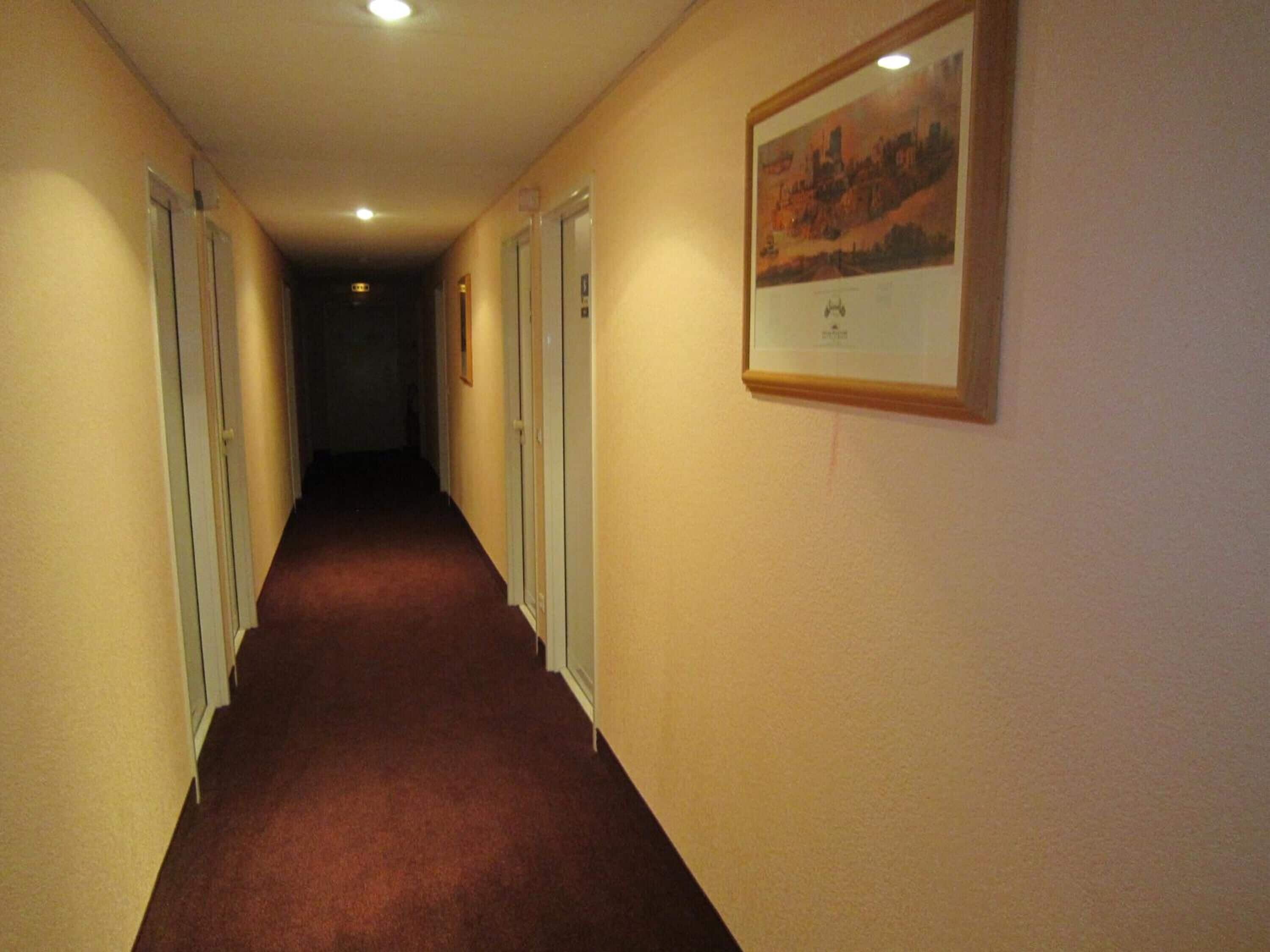 Ein schmaler Korridor mit Teppichböden, Türen auf beiden Seiten und einem gerahmten Bild an der rechten Wand.