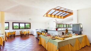 A dining area with tables, chairs, a buffet with food, and a television. - Petri Marini Hotel & Resort (Aglientu)
