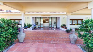 A hotel entrance with a tiled patio, large vases, and potted plants. - Petri Marini Hotel & Resort (Aglientu)