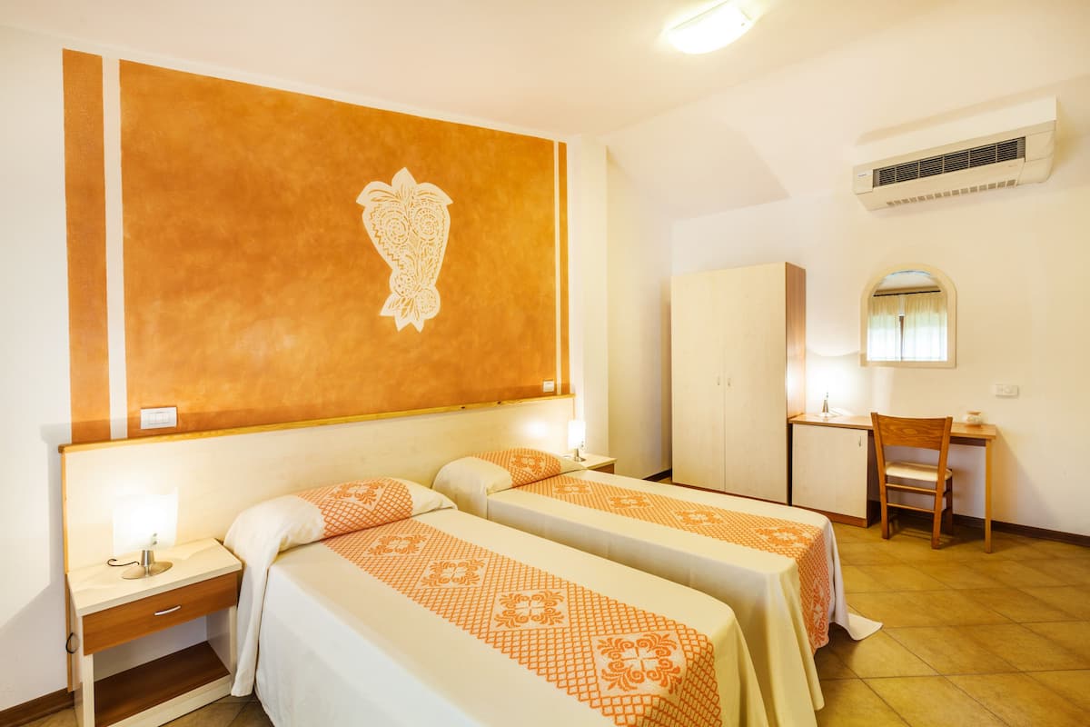 A hotel room with two beds, a desk, a chair, a wardrobe, and a large decorative wall piece.