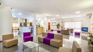 A spacious lobby with multiple seating areas, a reception desk, and a television. - Petri Marini Hotel & Resort (Aglientu)
