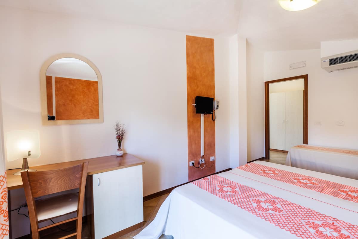 A hotel room with a bed, a desk, a chair, a mirror, and a wardrobe.