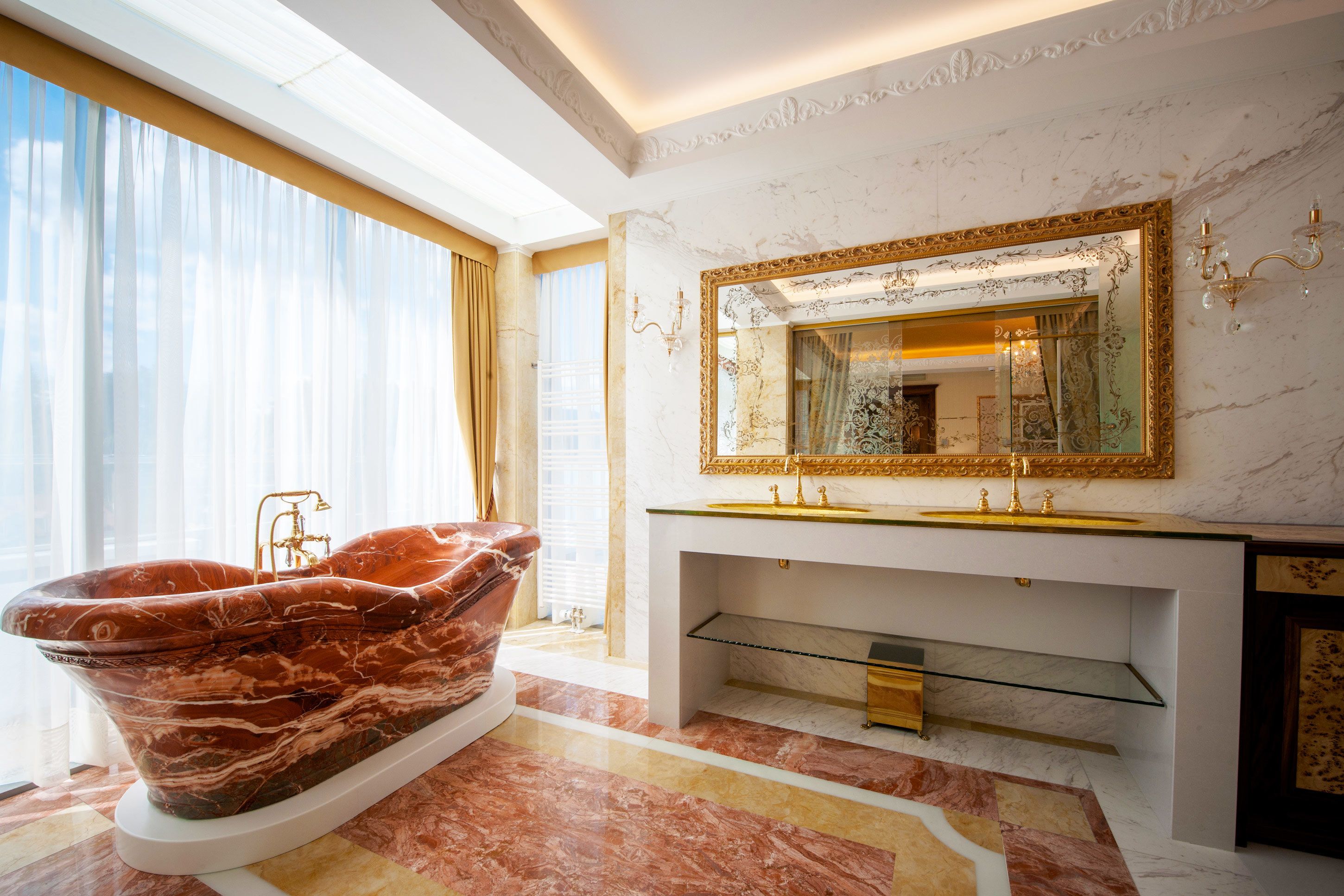 Un baño lujoso con una bañera de mármol, un espejo grande con un marco ornamentado y un tocador moderno.