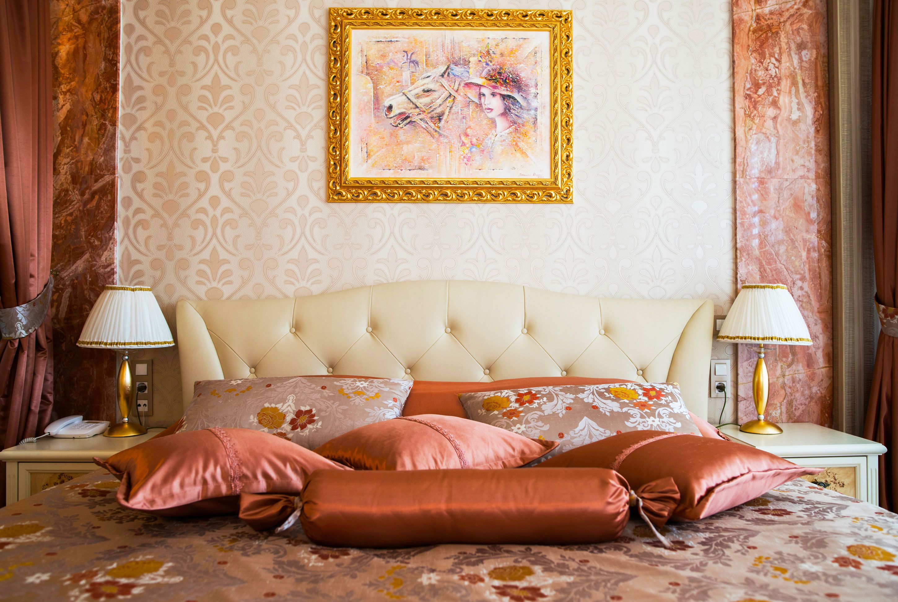Un dormitorio con cabecera capitonada, ropa de cama con estampado floral y dos lámparas de noche.