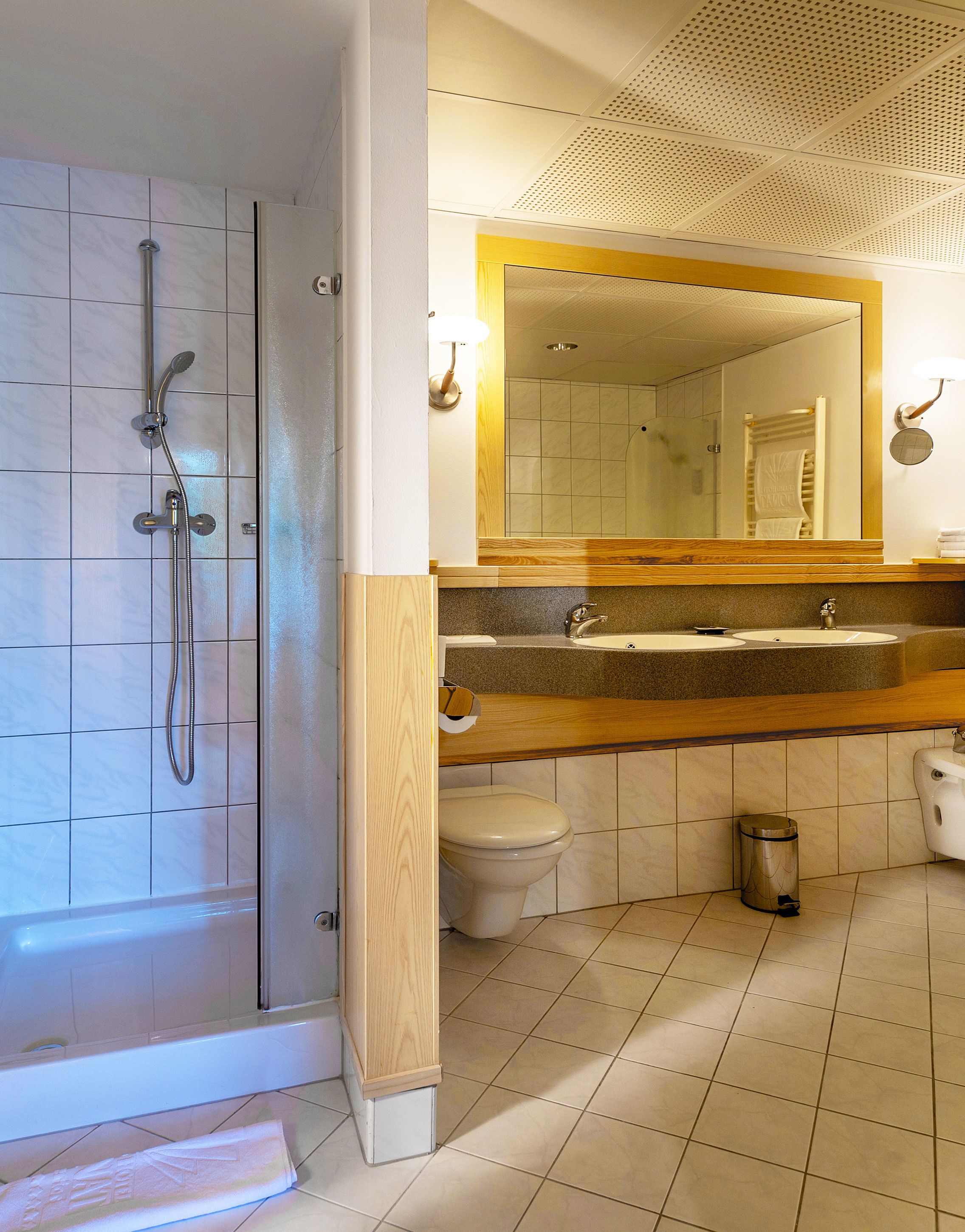 Un baño con ducha, inodoro, lavabo y un espejo grande.
