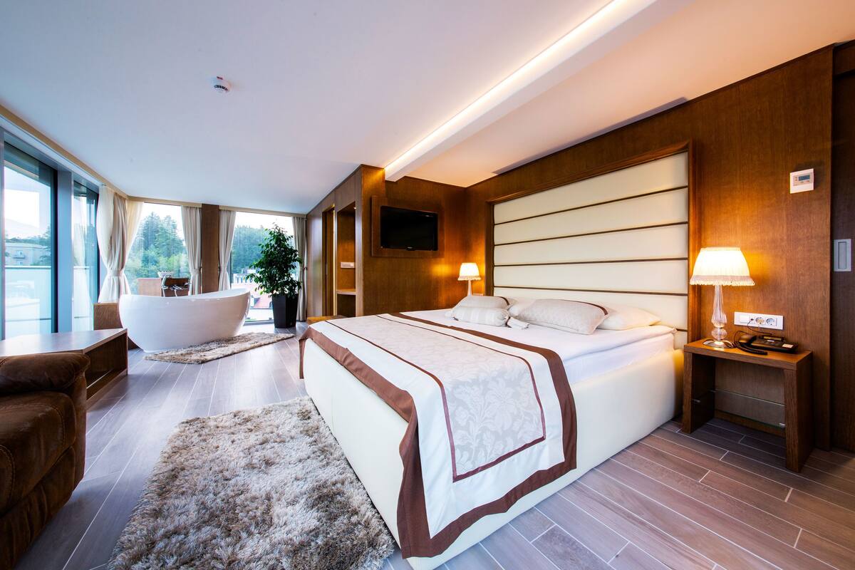 Une chambre d’hôtel moderne avec un grand lit, une baignoire, un canapé et un bureau avec une lampe.