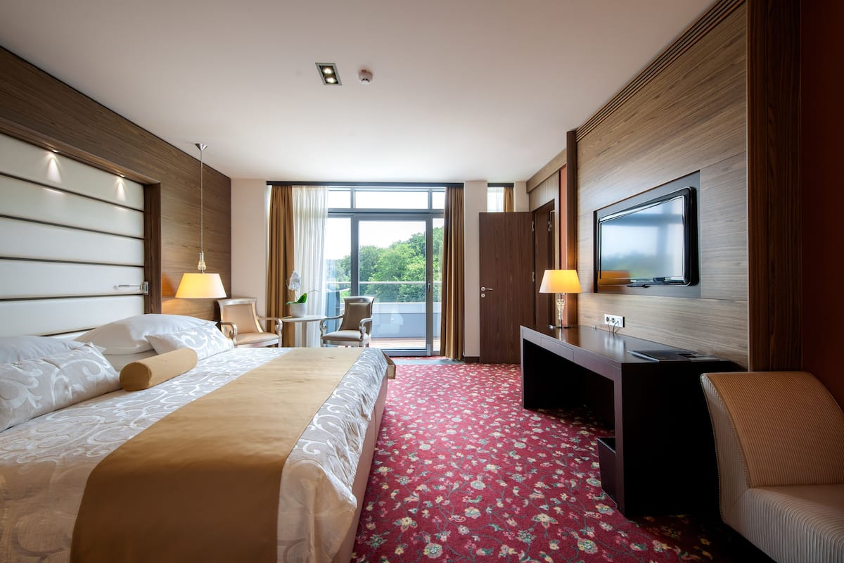 Une chambre d’hôtel avec un lit, un bureau, une télévision et un balcon offrant une vue.