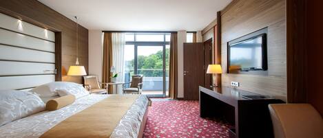 Una habitación de hotel con cama, escritorio, televisión y balcón con vistas.