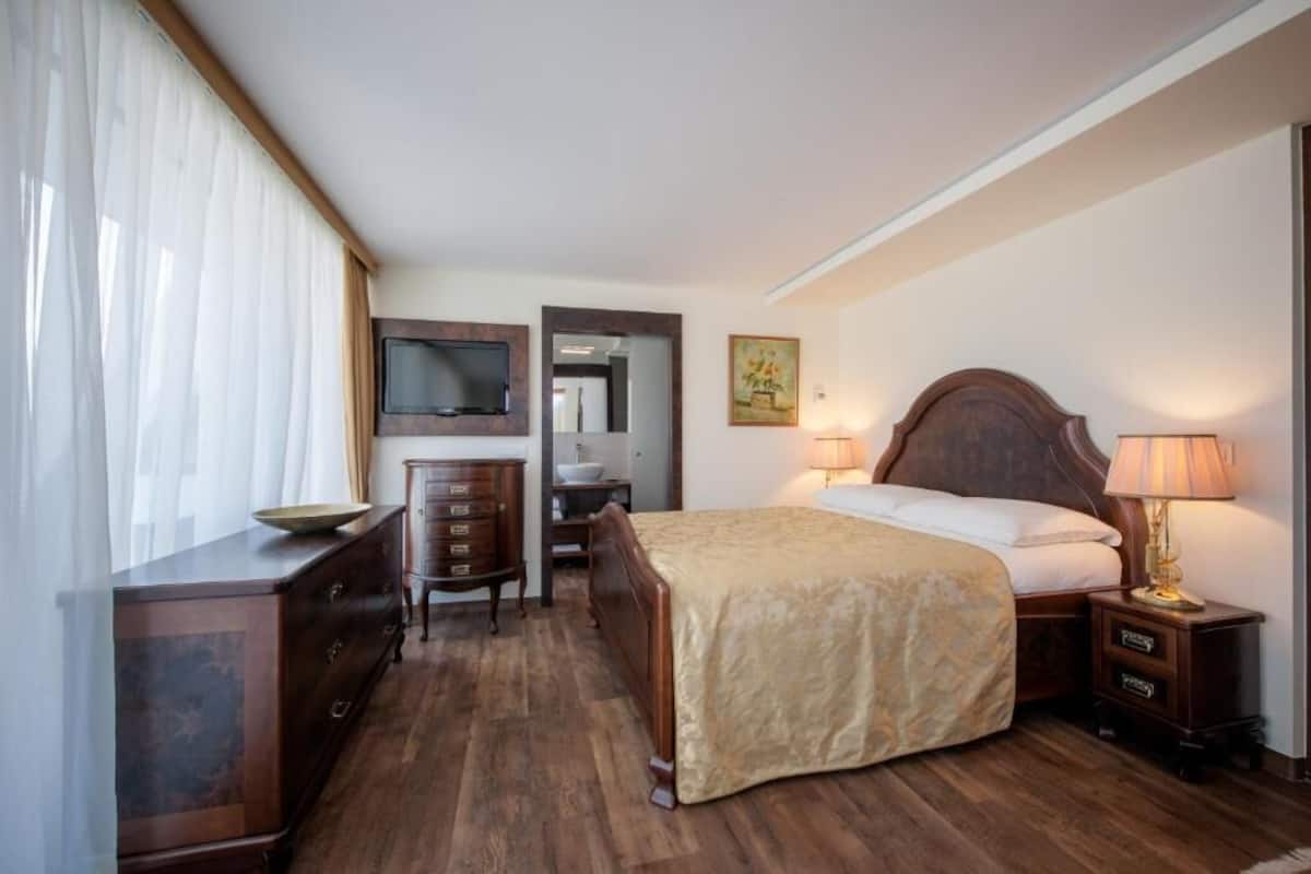 Une chambre d’hôtel avec un lit en bois, une commode, un bureau, une télévision et un tableau au mur.