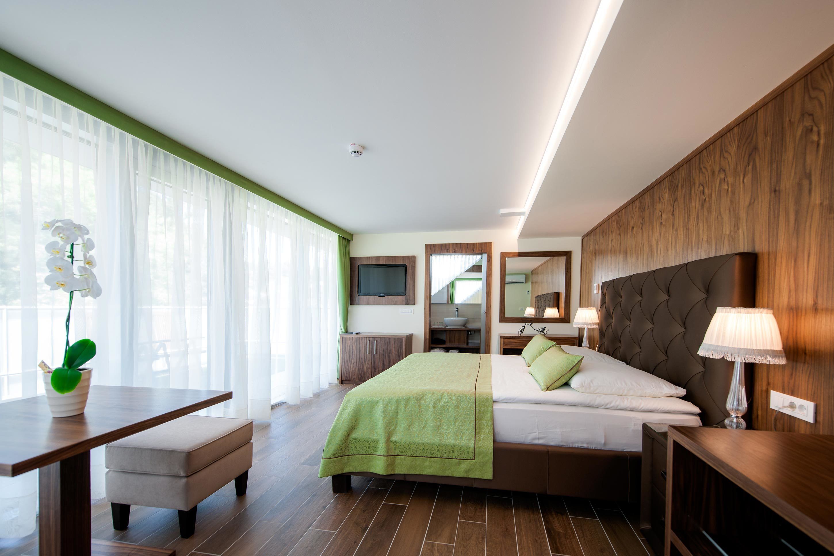 A modern hotel room with a large bed, a desk, and a green plant.
