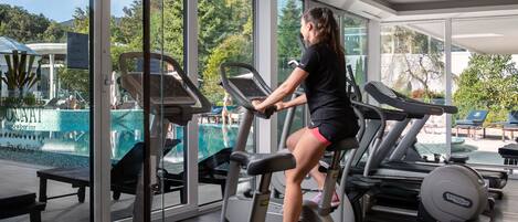 A gym with treadmills and exercise equipment, large windows, and a view of a pool and greenery.