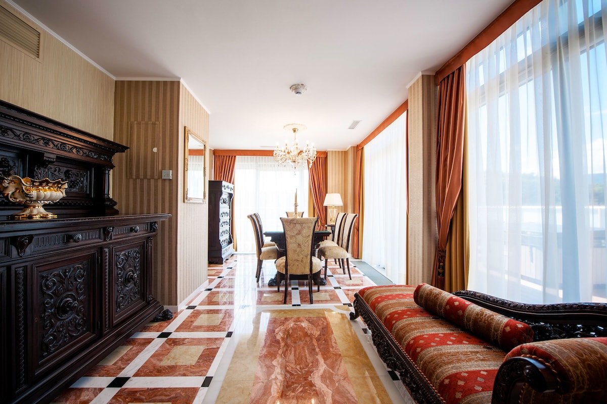 Une chambre d’hôtel avec un sol à carreaux, un canapé, une table à manger avec des chaises et un lustre.