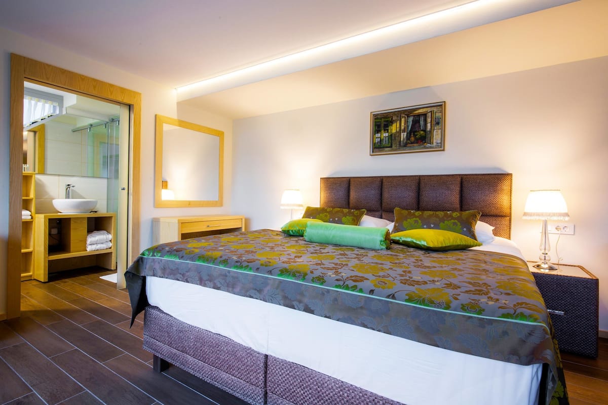 Une chambre d’hôtel moderne avec un grand lit, une salle de bain dotée d’une douche à parois de verre et un tableau au mur.