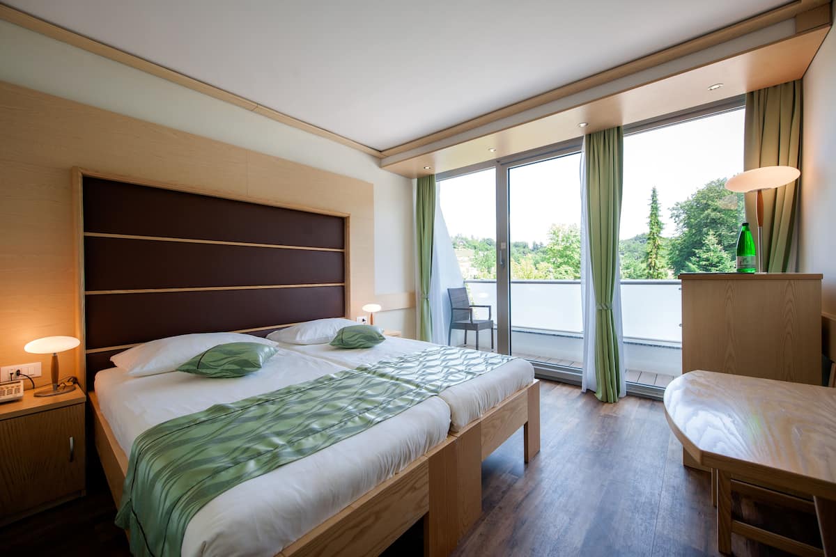 Une chambre d’hôtel moderne, dotée d’un grand lit, de tables de chevet, d’un bureau et offrant une vue sur l’extérieur.