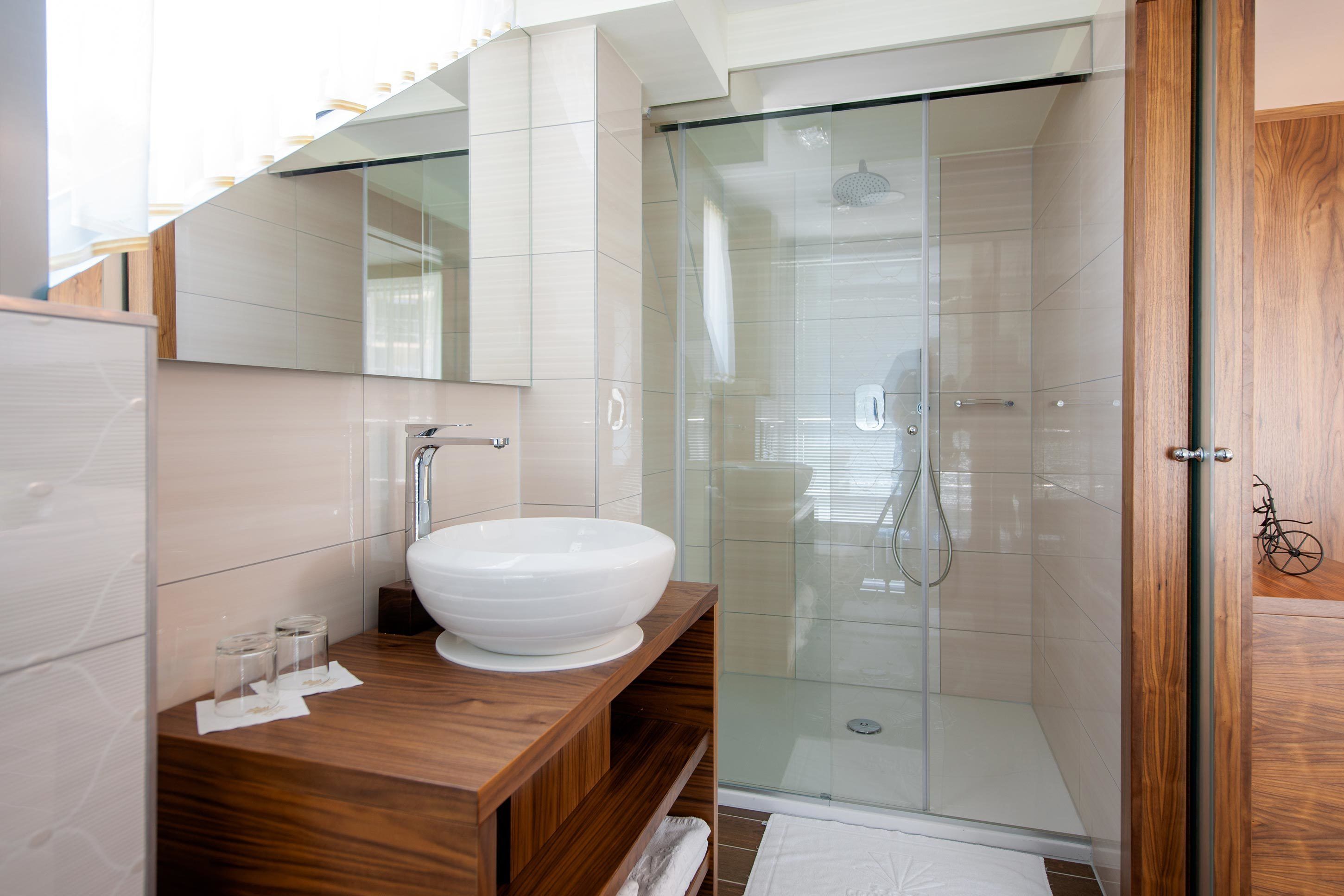 A modern bathroom with a large white sink, wooden vanity, and a glass-enclosed shower.