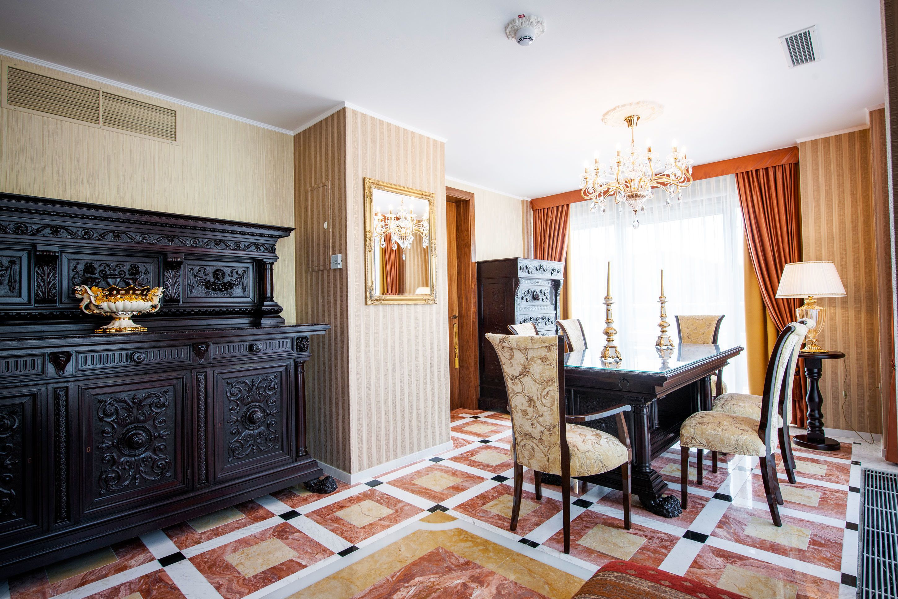 A dining area with a dark wooden buffet, a chandelier, and patterned chairs.