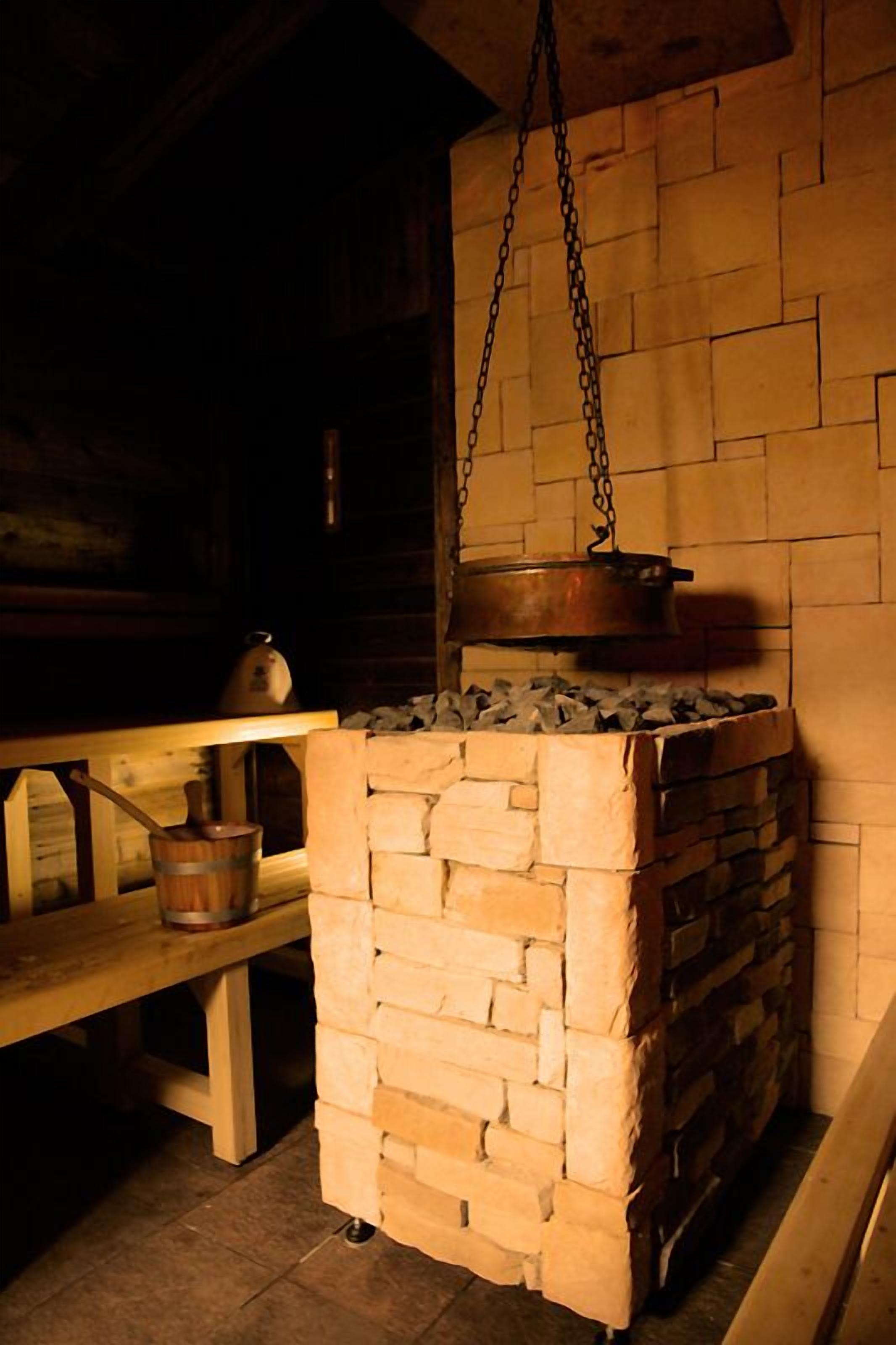 Una cocina rústica con un horno de ladrillo, una olla colgante y un banco de madera.