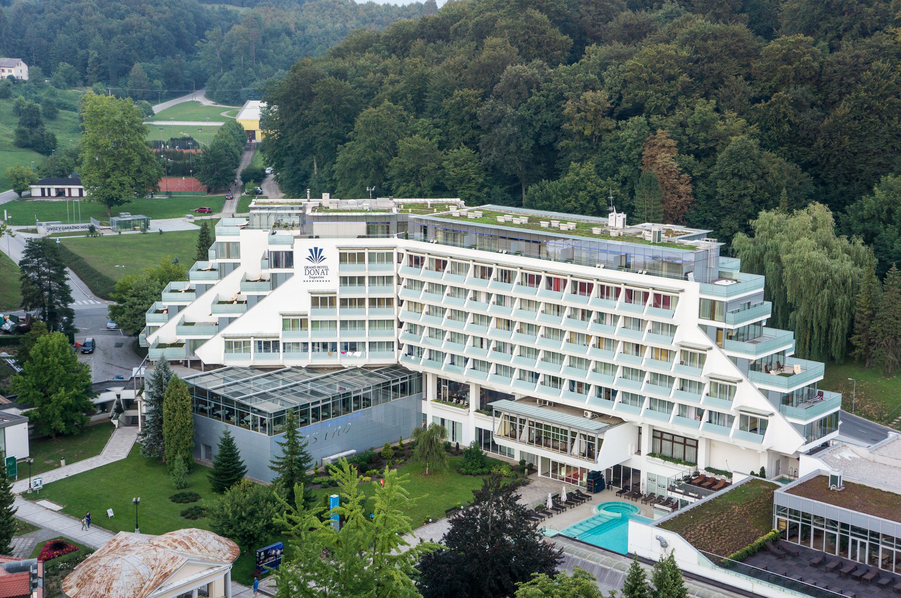 Un hotel moderno con varios pisos, una piscina y un entorno verde exuberante.