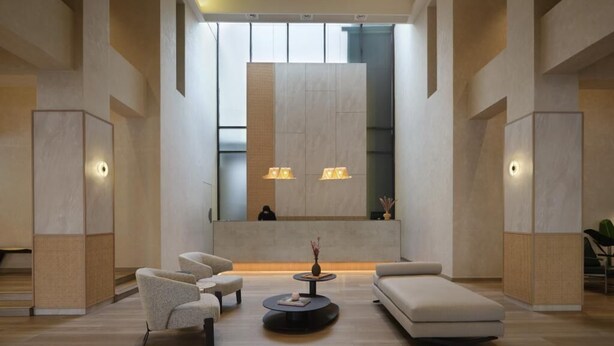 A modern lobby with a central seating area, a large wall with a recessed section, and a staircase to the left.