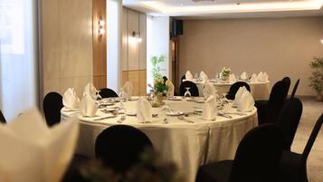 A conference room with round tables set for dining, black chairs, and a speaker system on the wall.