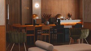 A modern hotel lobby with a wooden reception desk, a seating area with green upholstered chairs, and a large vase with dried plants.