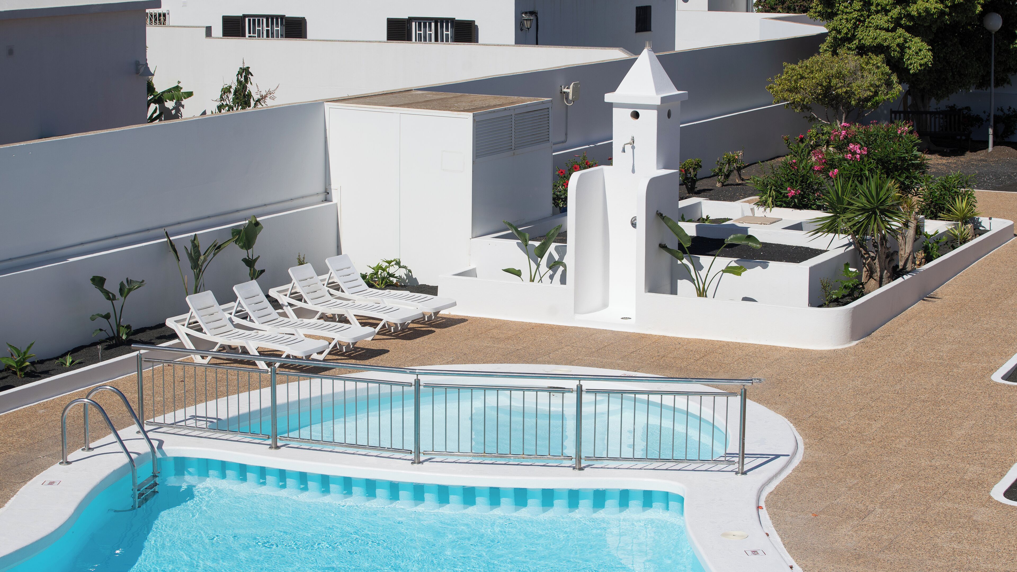 Una piscina con sillas de descanso, rodeada de paredes blancas y plantas.
