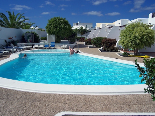 Una piscina con agua azul cristalina, rodeada de sillas de descanso y plantas en macetas.