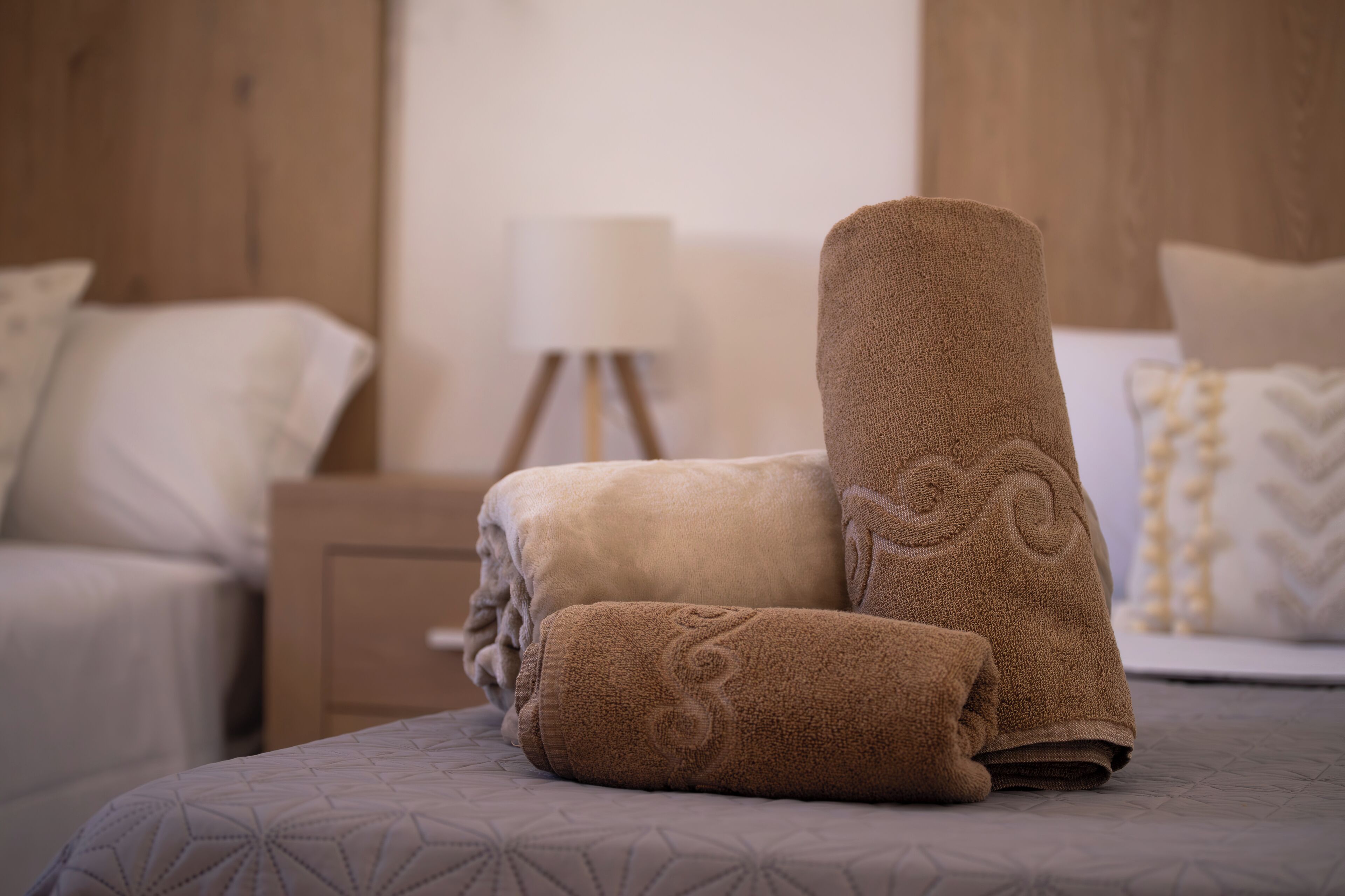 A neatly made bed with a patterned bedspread, a wooden nightstand with a lamp, and a wall with a textured finish.