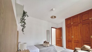 Een slaapkamer met twee bedden, een houten kledingkast, een hangplant en een plafondventilator.