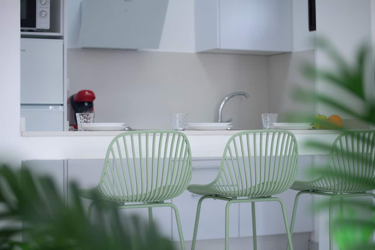 Una cocina moderna con armarios blancos, un lavamanos de acero inoxidable y sillas verdes.