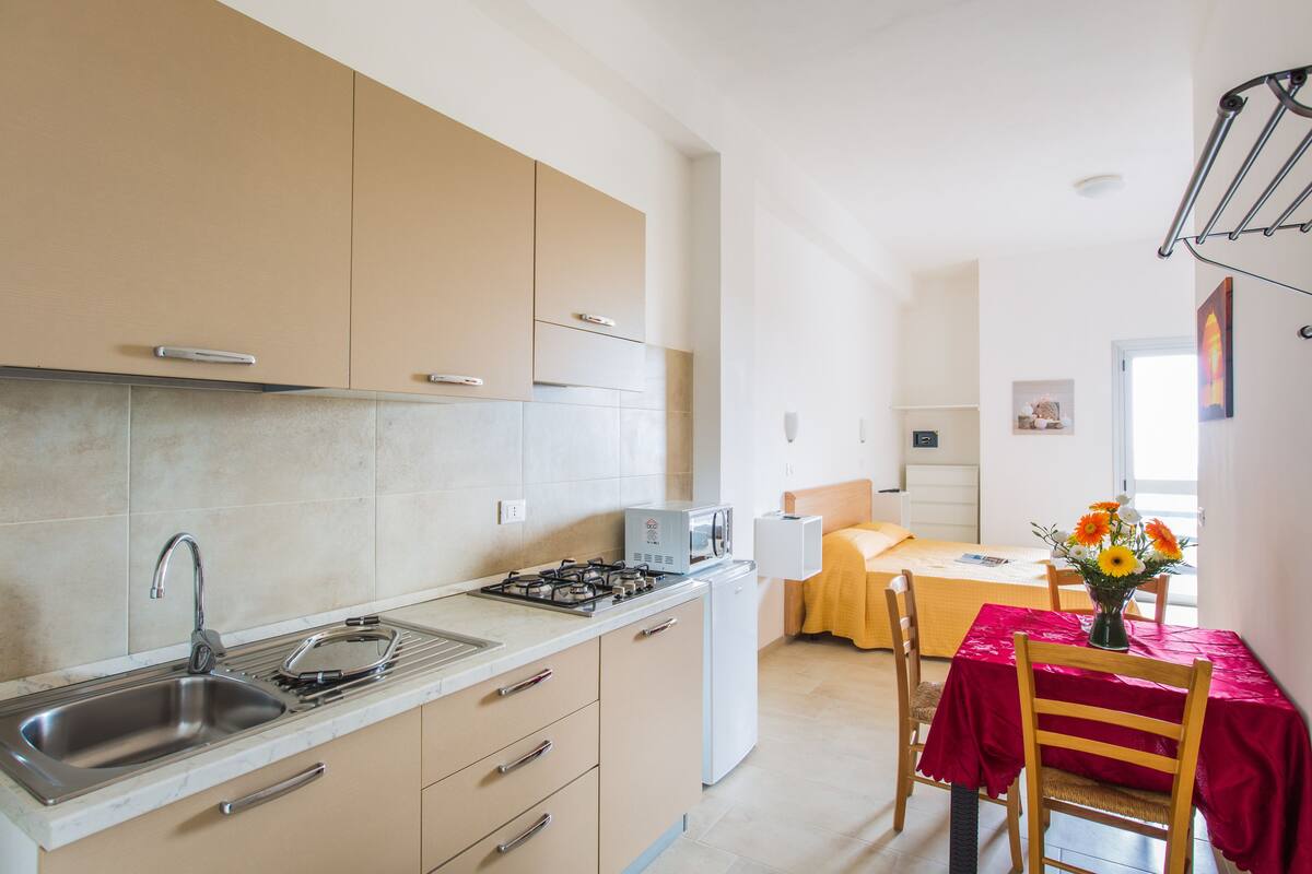 A modern kitchen with a sink, stove, and microwave. There is a dining area with a table and chairs, and a window with a view.