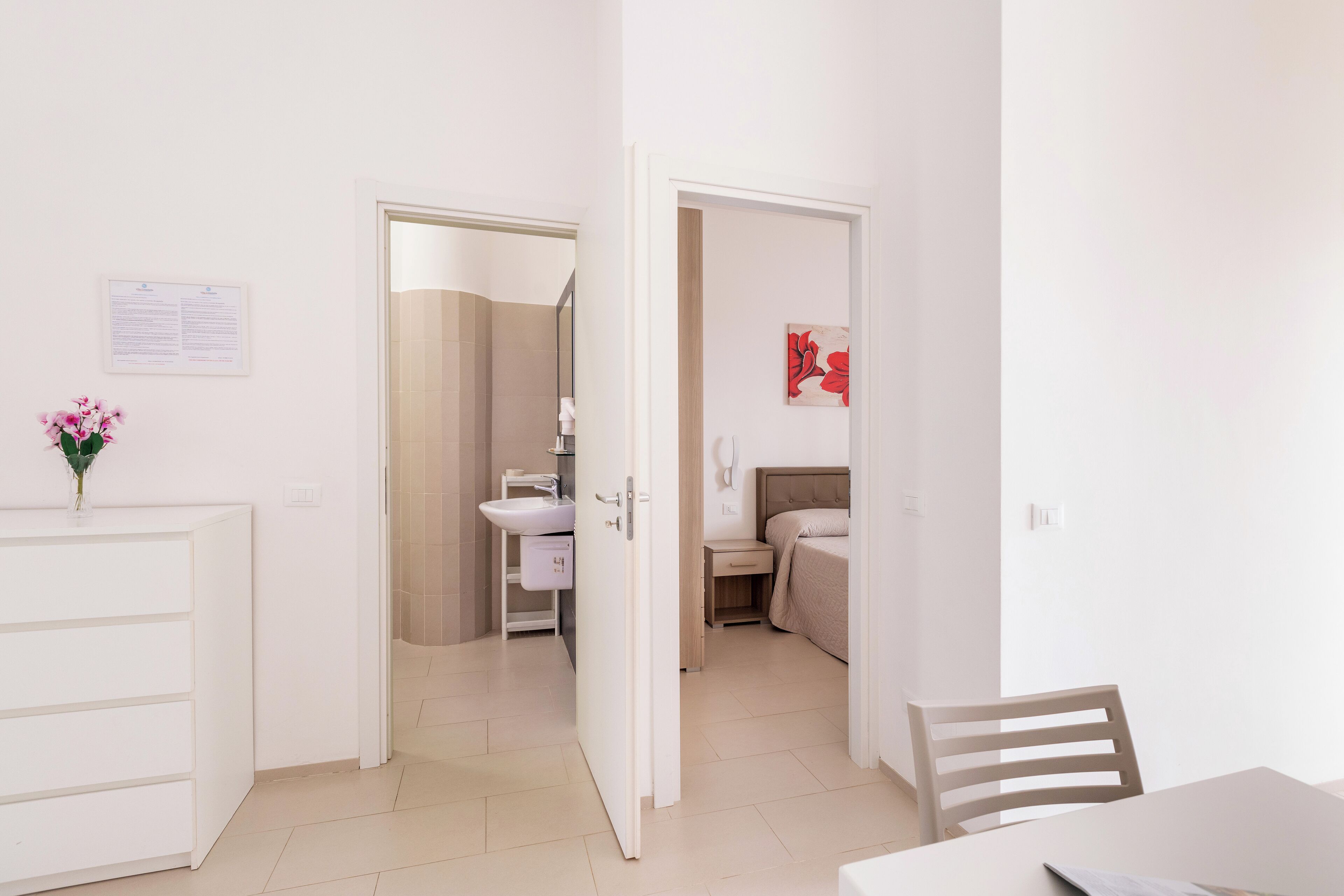 Hotellihuone, jossa on sänky, yöpöytä sekä kylpyhuone, jossa on pesuallas ja peili.