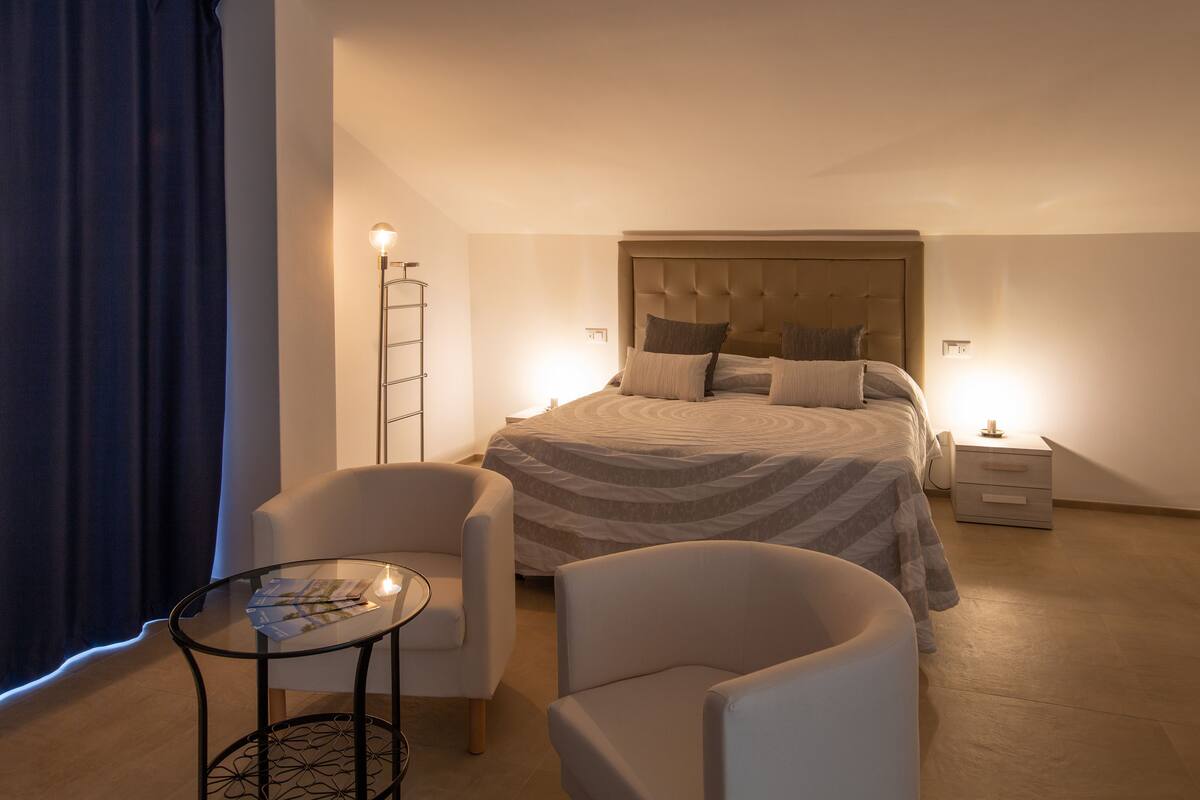 A bedroom with a bed, two bedside tables, a chair, a small table, and a floor lamp.