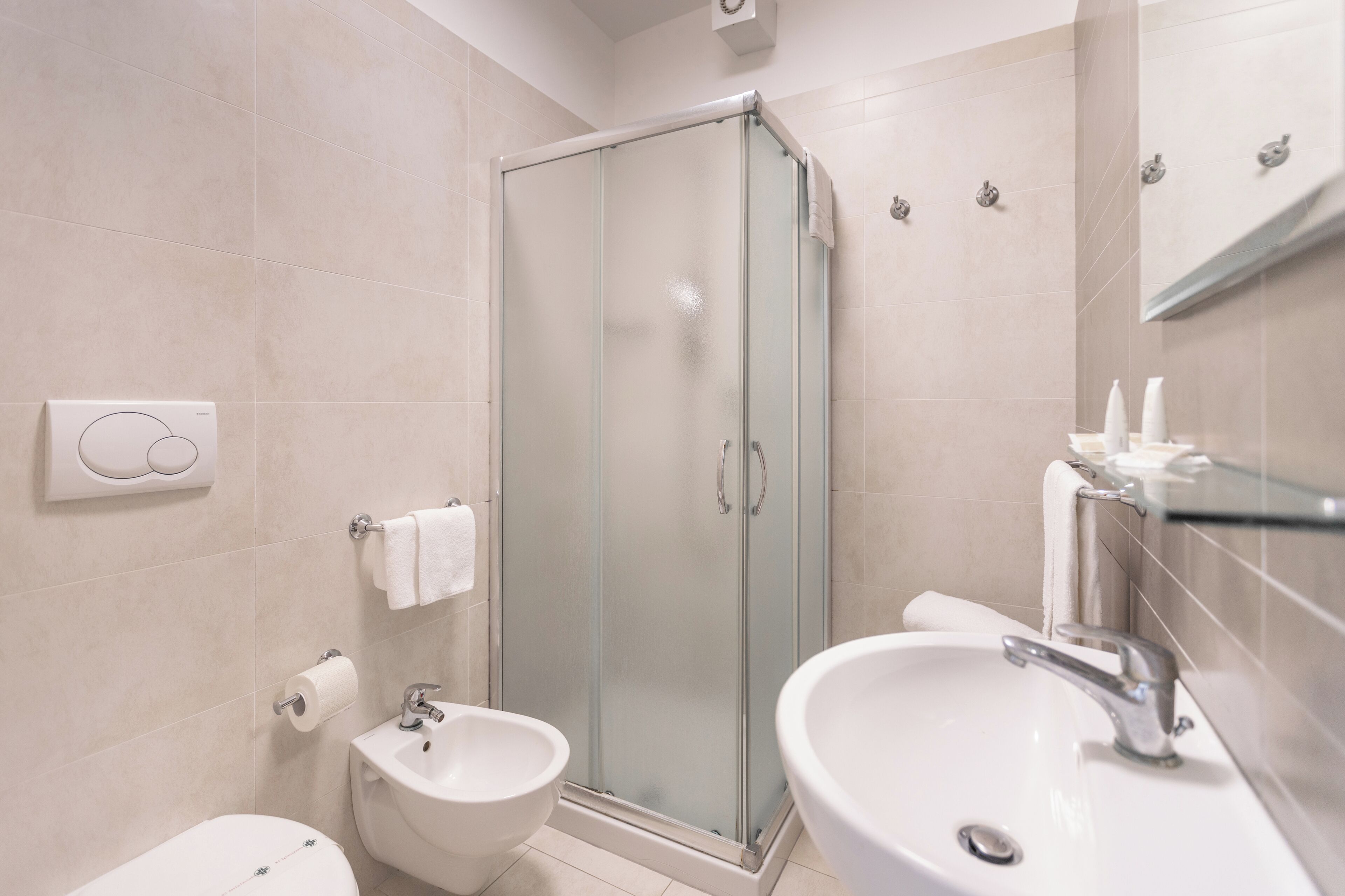 Een moderne badkamer met een douchecabine van glas, een bidet, een wastafel en een toilet.