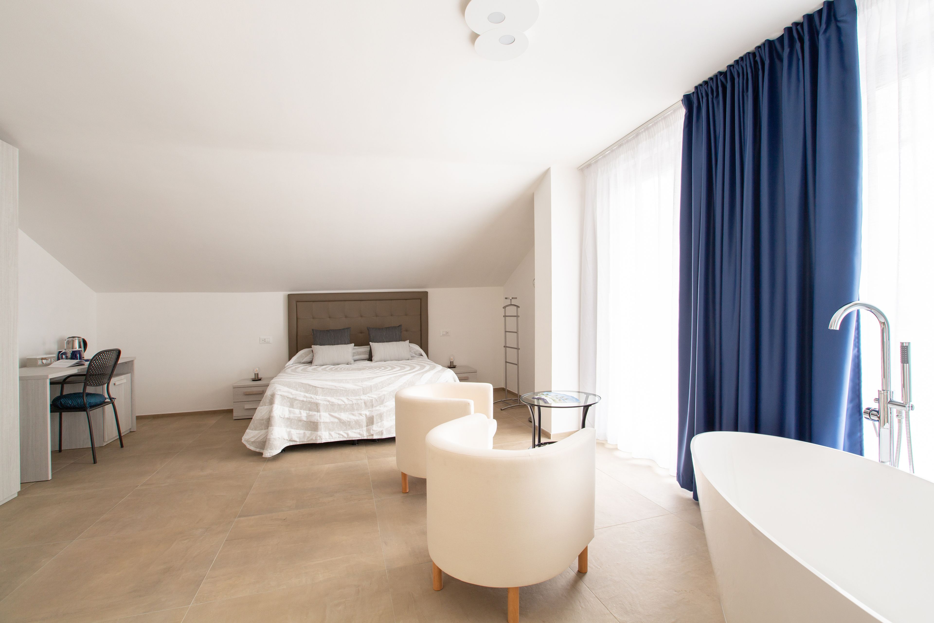 Un dormitorio moderno con una cama, dos sillones blancos, un escritorio y un baño con bañera.