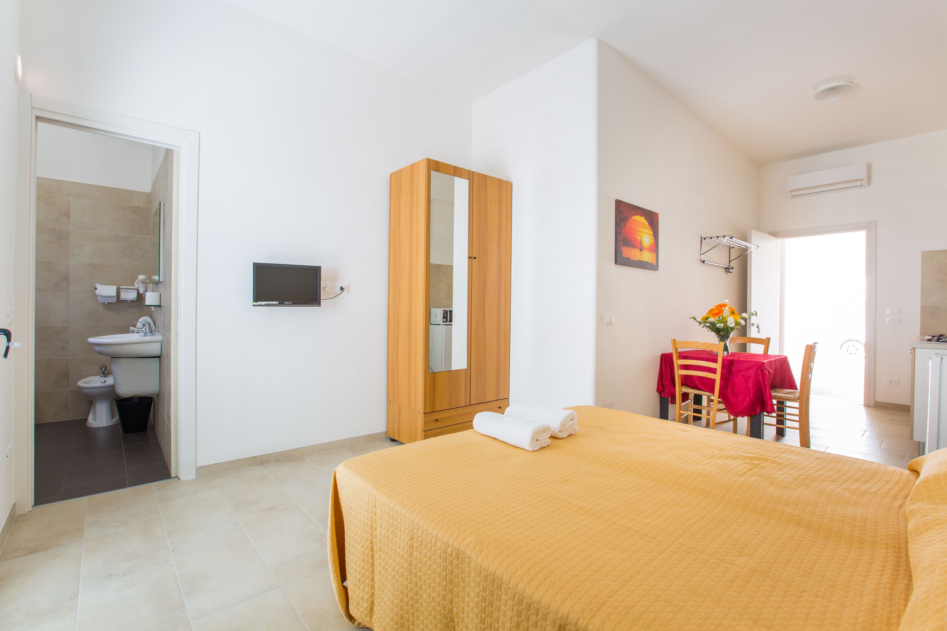 A hotel room with a bed, a TV, a bathroom, and a dining area.