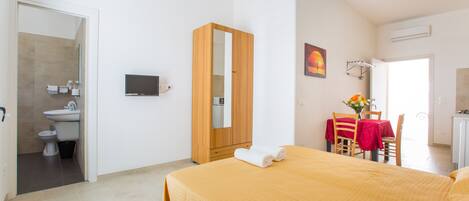 A hotel room with a bed, a TV, a bathroom, and a dining area.