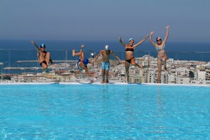 A swimming pool with clear blue water, surrounded by a cityscape with buildings and a view of the sea. - Villa Coppitella  Rooms & Apartments (Vieste)