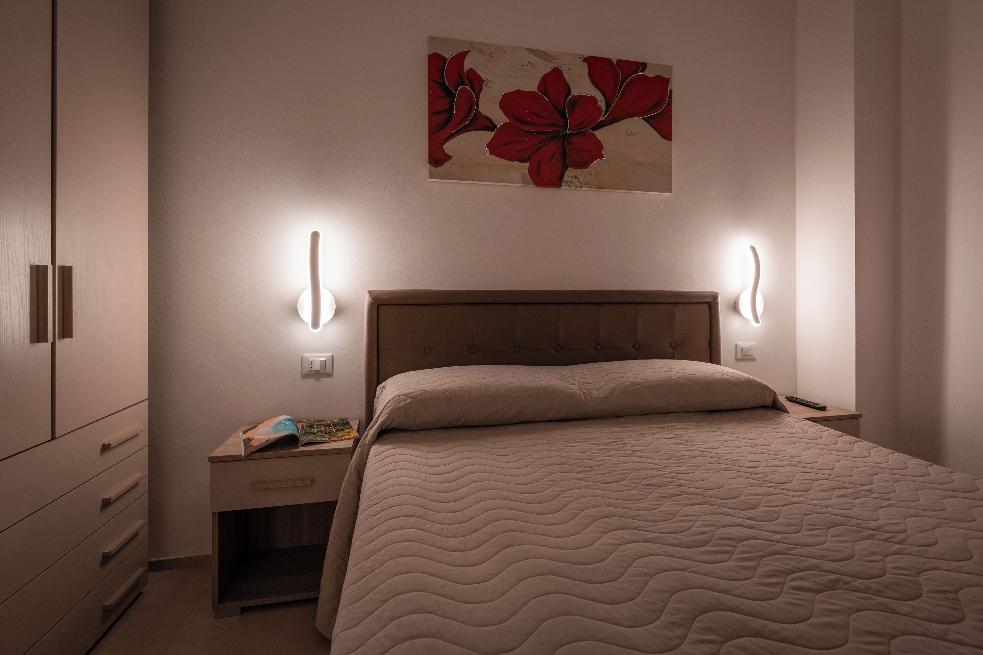 A bedroom with a bed, nightstands, a dresser, and a wall-mounted artwork.
