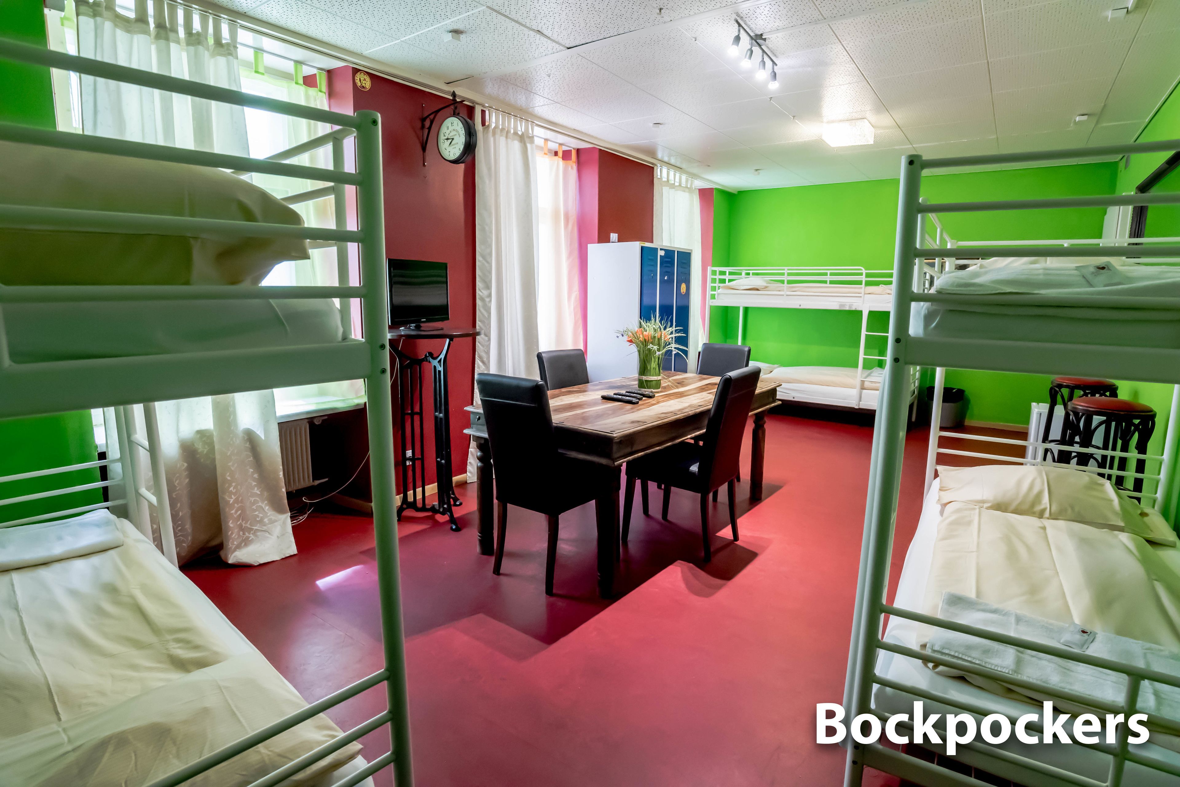 A dormitory room with bunk beds, a dining table with chairs, a clock, and a radiator.