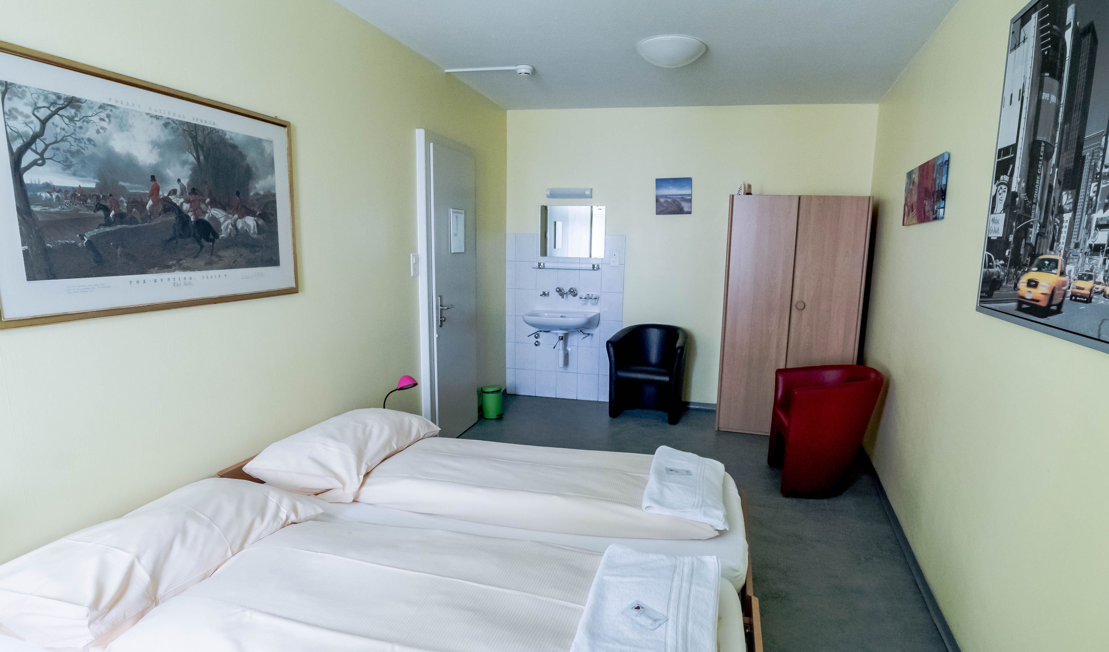 Ett hotellrum med en säng, ett handfat, en garderob och en inramad tavla på väggen.