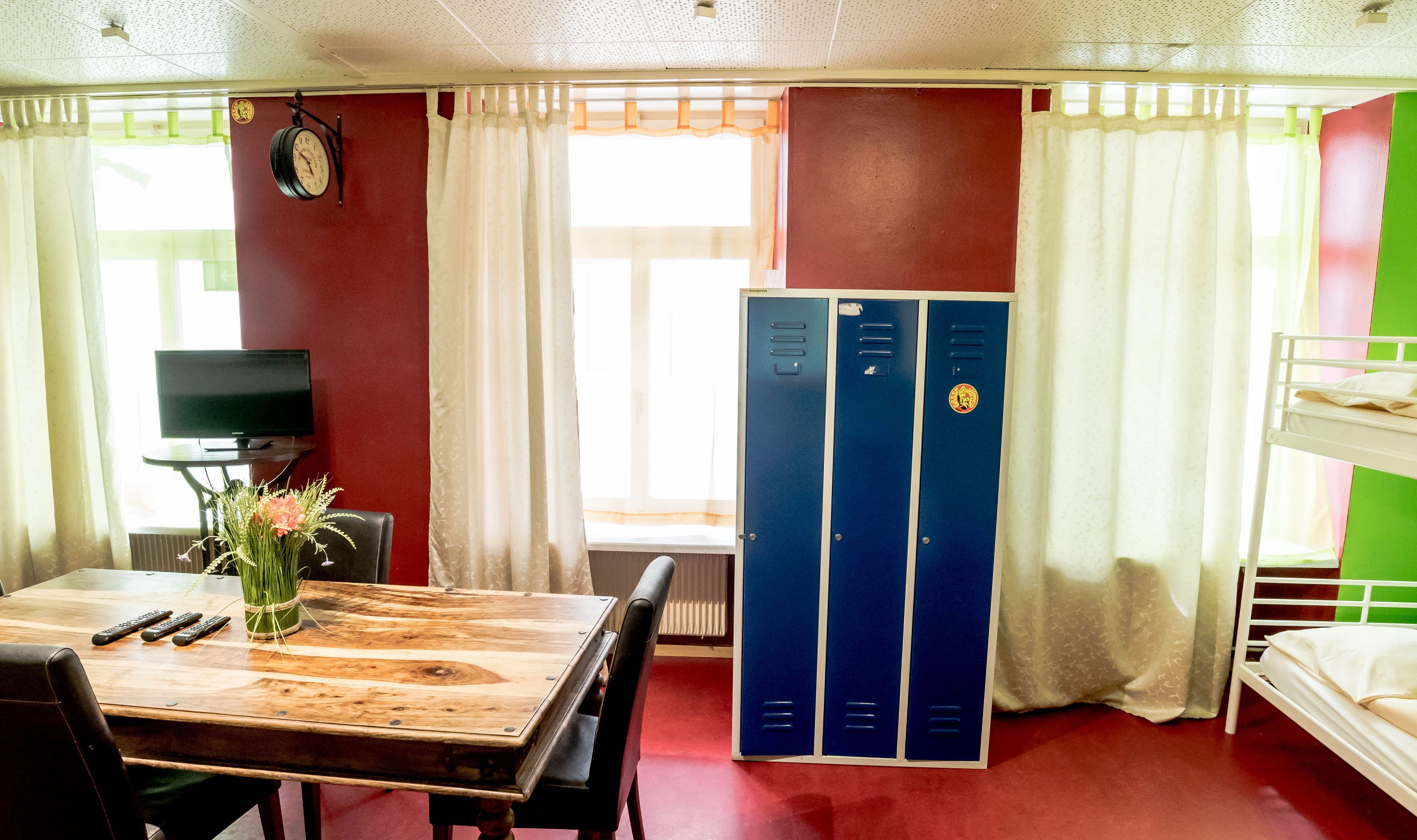 Ein Zimmer mit Holztisch, Fernseher, Uhr und Etagenbett.