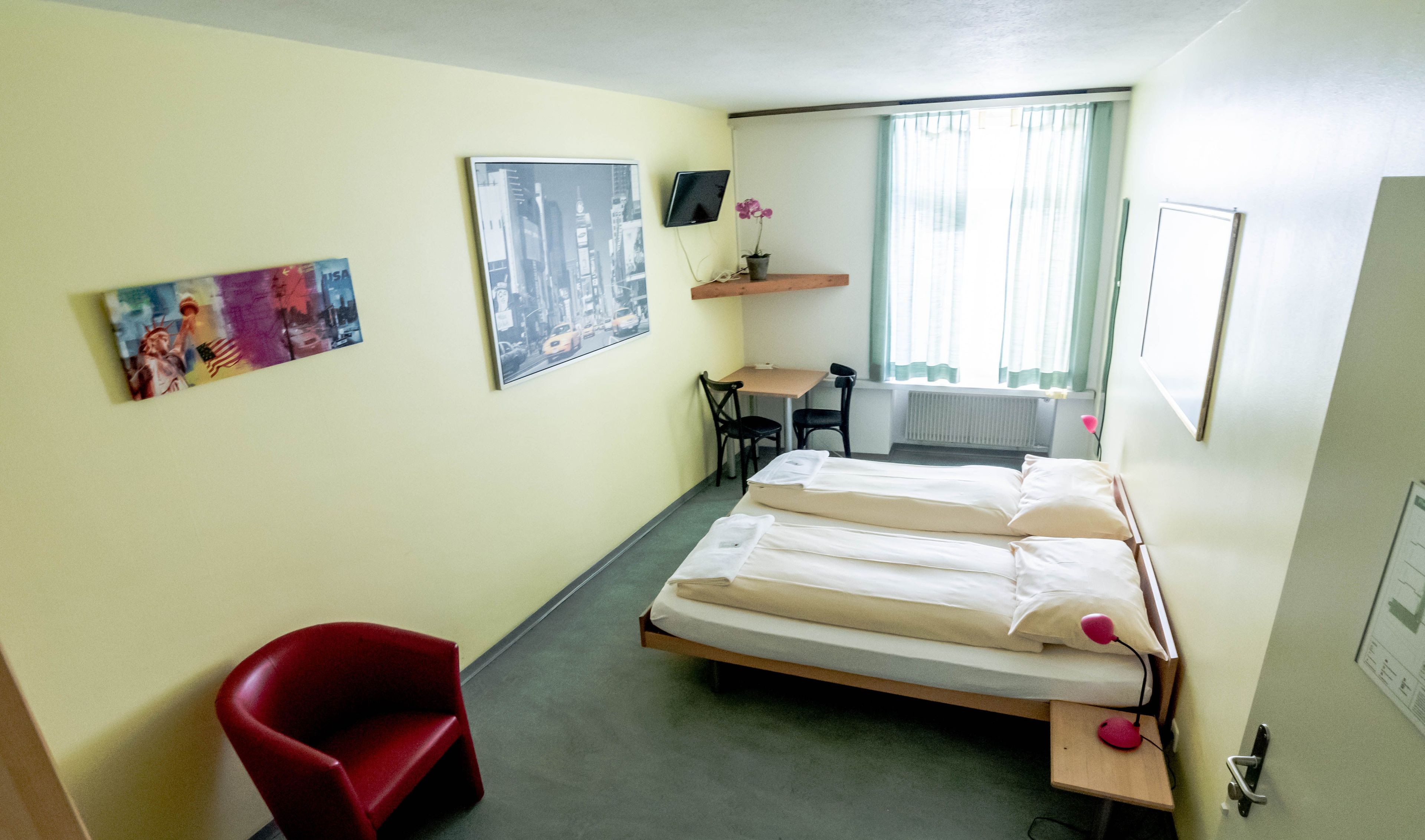 Une chambre d’hôtel avec un lit, un bureau, une chaise et un téléviseur fixé au mur.