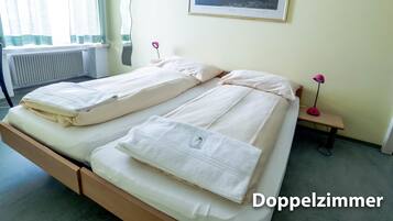 Habitación doble con cama, mesita de noche, lámpara y un cuadro en la pared.