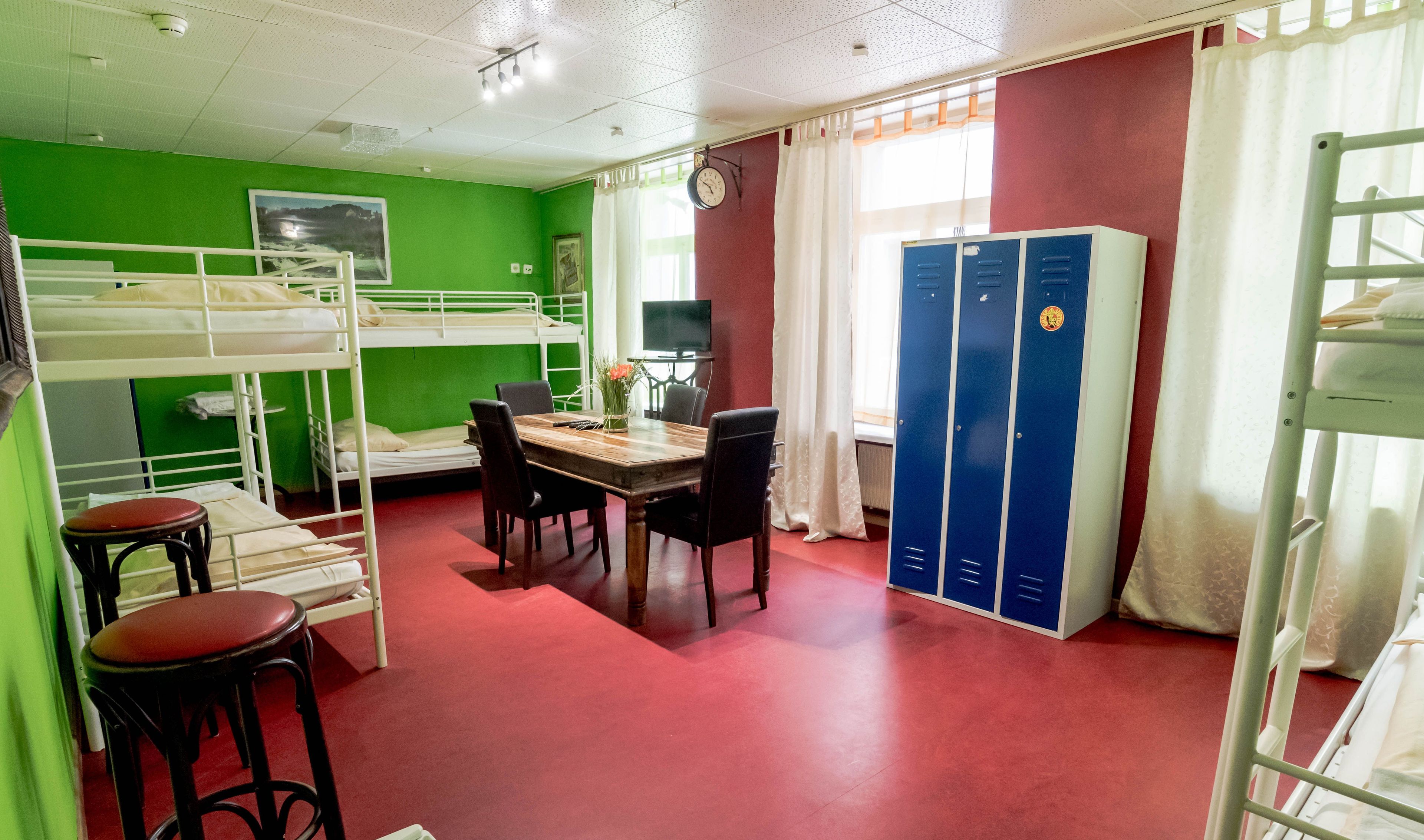Ein Schlafsaalzimmer mit Etagenbetten, einem Esstisch mit Stühlen, einer Uhr und Schließfächern.